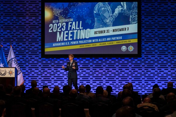 A woman in uniform on stage speaks to a crowd sitting down.