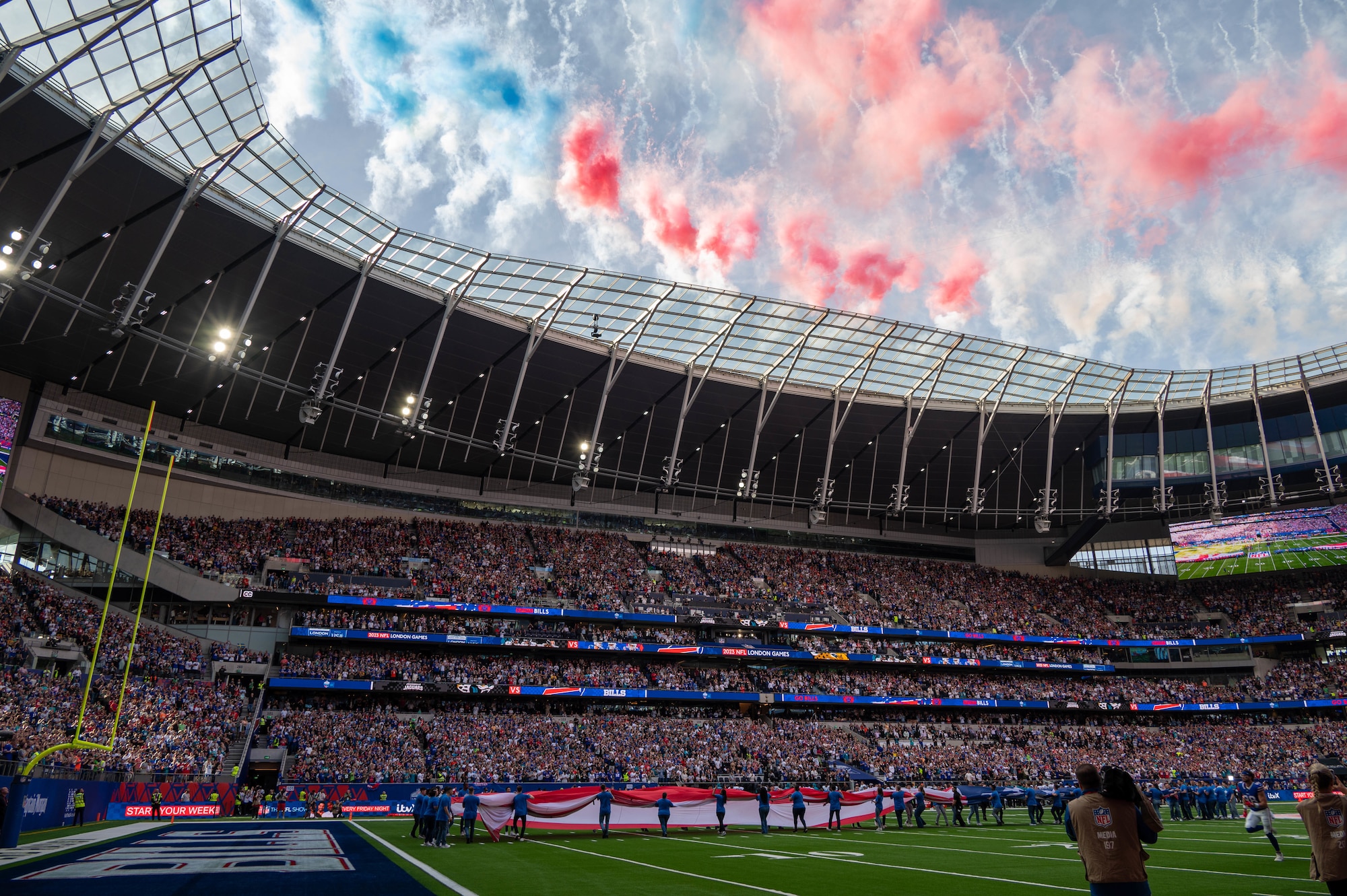 61,000 football fans cheer before the start of a football game while red, white and blue smoke rises behind them