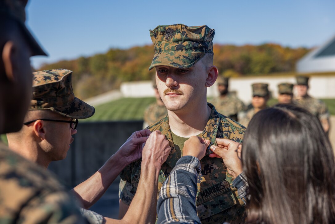 U.S. Marine Corps Sgt. Kedrick Schumacher, a combat graphics specialist with Security Battalion, and a Wasilla, Alaska native, has his sergeant chevrons placed on him by Katie Schumacher, his wife, and GySgt. Dustin March, a Communication Strategy and Operations operations chief, during his promotion ceremony at the National Museum of the Marine Corps, Virginia, Nov. 1, 2023. Promotion ceremonies are a significant achievement in a service member’s career and are a testament to their commitment, mastery of duties and skills, and leadership capabilities. (U.S. Marine Corps photo by Lance Cpl. Ethan Miller)