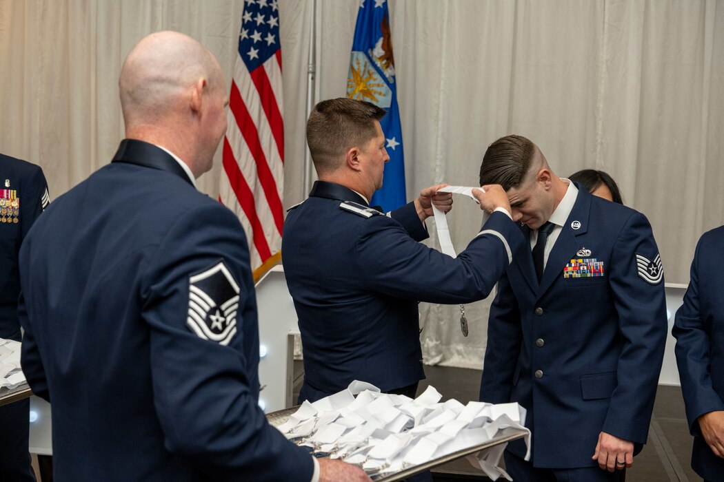 An Airman places a medallion around another Airman's head.