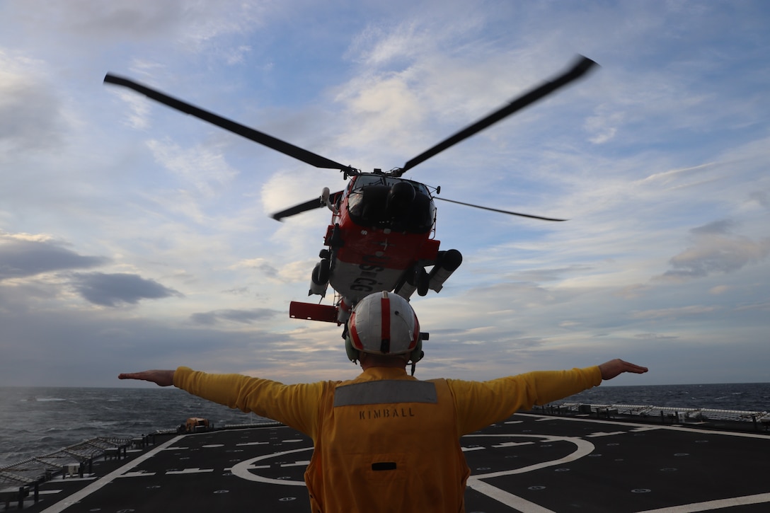 U.S. Coast Guard Cutter Kimball (WMSL 756) crewmember Ensign Phil Rogers relays hand signals to an aircrew while conducting flight operations near Cold Bay, Alaska with a HH-60 Jayhawk from Air Station Kodiak, Oct. 12, 2023. To ensure crew preparation and proficiency, Kimball conducted numerous flight operations with MH-65 Dolphin and HH-60 Jayhawk helicopters and aircrews from U.S. Coast Guard Air Station Kodiak, resulting in the qualification of eight pilots and recertification of Kimball's crew. U.S. Coast Guard photo by Seaman Reese Sipos.