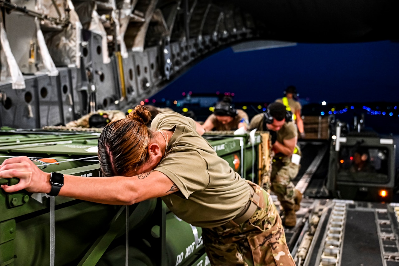 Service members push metal crates onto an aircraft.