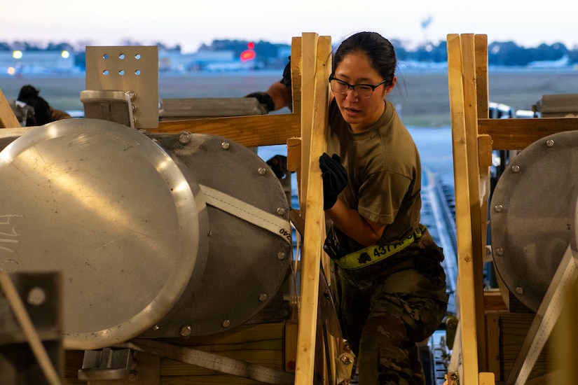 A service member pushes equipment in a wooden frame up a ramp of an aircraft.