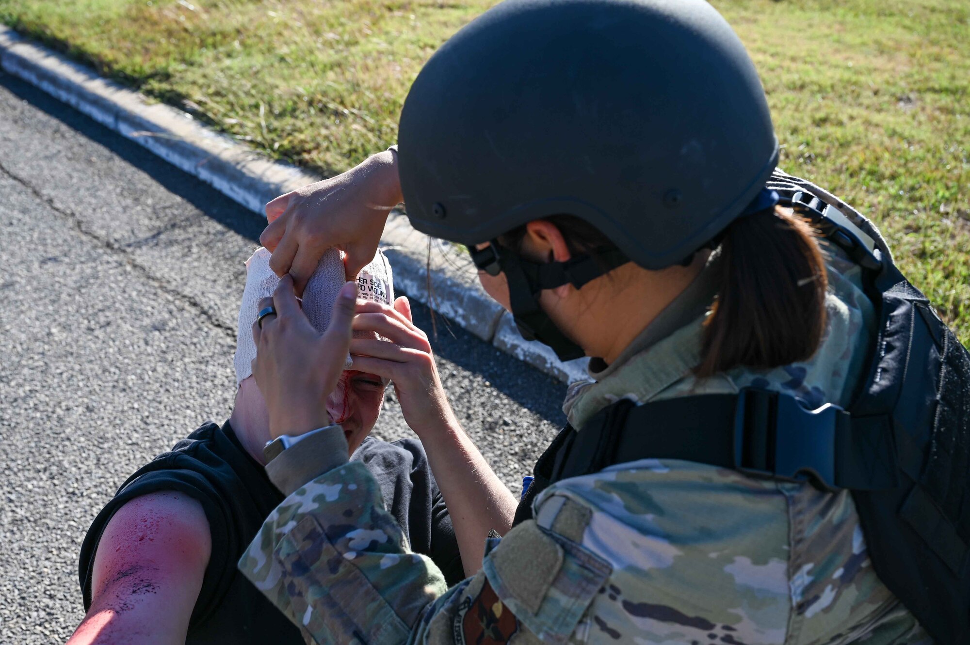 U.S. Air Force Master Sgt. Brenda Khamthingath, 97th Medical Group bioenvironmental engineering flight chief, fashions a head wrap around a patient during the Caduceus Spear exercise at Clinton Sherman Airfield Park, Oklahoma, Oct. 26, 2023. This type of wrap is common to us during Tactical Combat Casualty Care. (U.S. Air Force photo by Airman 1st Class Kari Degraffenreed)