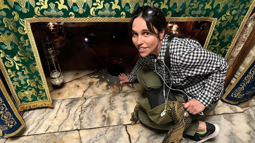 A woman crouches down to a stone floor near a religious relic