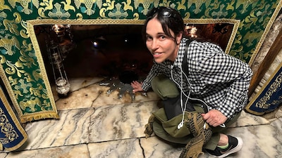 A woman crouches down to a stone floor near a religious relic