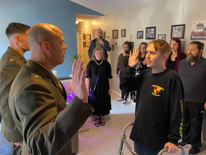 A Marine Corps general raises his right hand and faces a civilian doing the same in a family home as others watch.