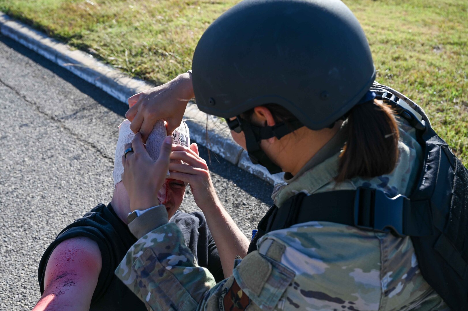 U.S. Air Force Master Sgt. Brenda Khamthingath, 97th Medical Group bioenvironmental engineering flight chief, fashions a head wrap around a patient during the Caduceus Spear exercise at Clinton Sherman Airfield Park, Oklahoma, Oct. 26, 2023. This type of wrap is common to us during Tactical Combat Casualty Care. (U.S. Air Force photo by Airman 1st Class Kari Degraffenreed)