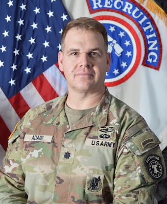 male Soldier posed in front of two flags.