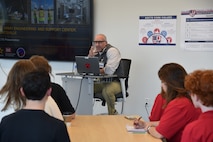 Chad House, a Huntsville Center engineer, sits behind a desk whill speaking to students at Alabama School of Cyber Technology and Engineering Oct. 27. The Huntsville-located charter school is ranked academically in the top 1% of U.S. high schools and is the nation’s only high school focused on the integration of cyber technology and engineering into all academic disciplines.