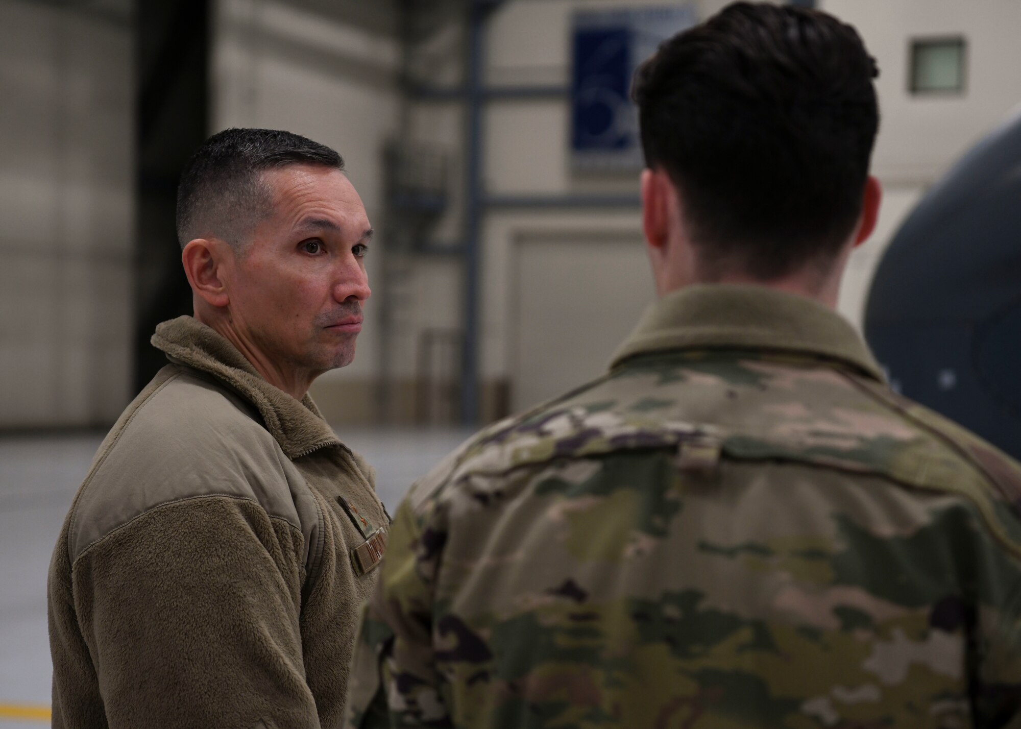 Two men in green uniforms talk with each other.