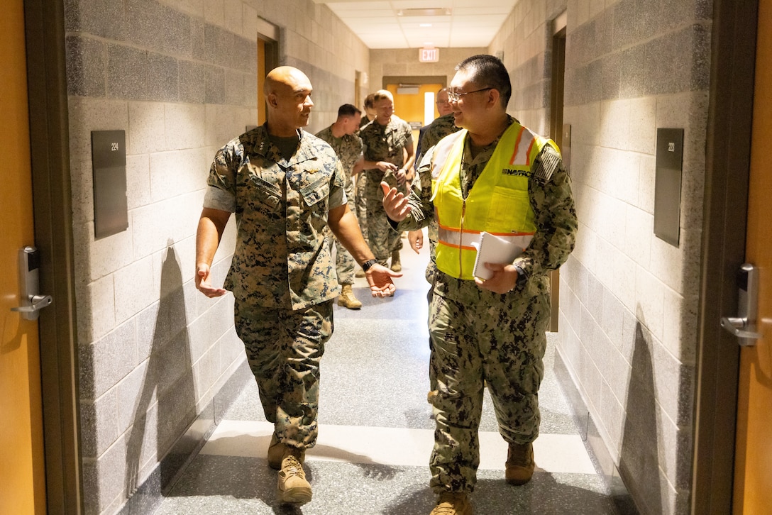 Two Marines in combat uniforms walking and talking together in a barracks hallway.