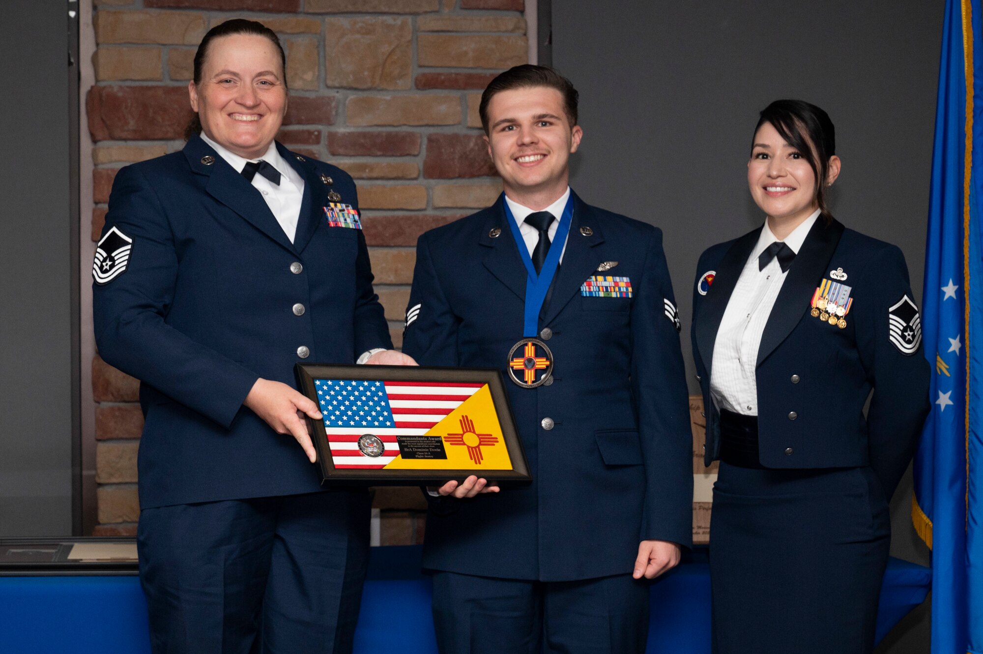 U.S. Air Force Senior Airman Dominic Devio, center, Airman Leadership Graduate, accepts the Commandant’s Award from U.S. Air Force Master Sgt. Angela McAllister, left, and U.S. Air Force Master Sgt. Cecilia Ayon during the graduation of Joel C. Mayo Class 24-A at Holloman Air Force Base, New Mexico, Nov. 2, 2023. The Commandant’s award is selected by the ALS commandant and is presented to the student who best demonstrates the characteristics of an effective leader. (U.S. Air Force photo by Airman 1st Class Michelle Ferrari)