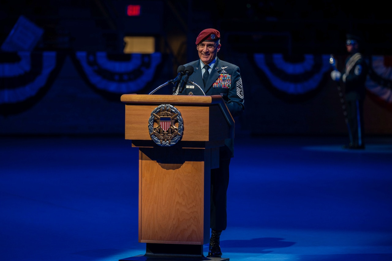 A uniformed service member smiles while standing at a lectern.