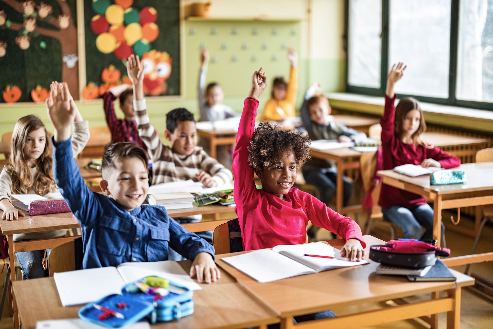 Photo of primary school classroom with children raising hands.