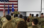 A man in a green military uniform speaks to a crowd of people in green military uniforms.