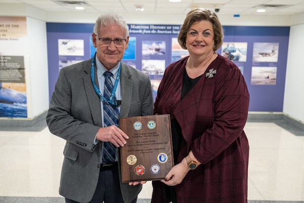 A man and woman are photographed holding a wooden plaque.