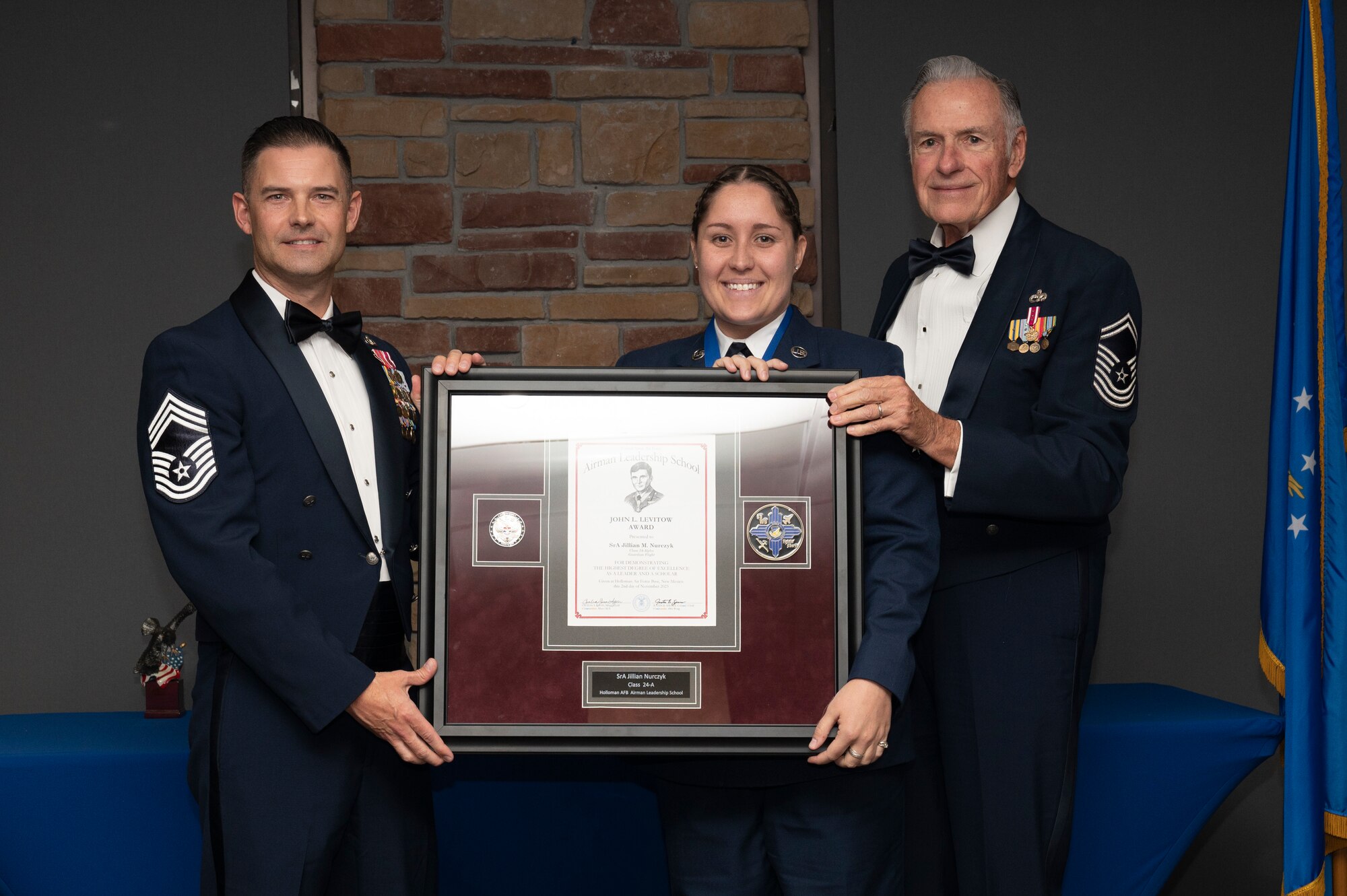 U.S. Air Force Senior Airman Jillian Nurczyk, center, Airman Leadership Graduate, accepts the John L. Levitow Award from Chief Master Sgt. Joshua Ziriak, left, and Retired Chief Master Sgt. Richard McElderry, during the graduation of Joel C. Mayo ALS Class 24-A at Holloman Air Force Base, New Mexico, Nov. 2,, 2023. The John L. Levitow award is presented to the student demonstrating the highest level of leadership and scholastic performance and is partially determined by the assignment of points by their peers. (U.S. Air Force photo by Airman 1st Class Michelle Ferrari)