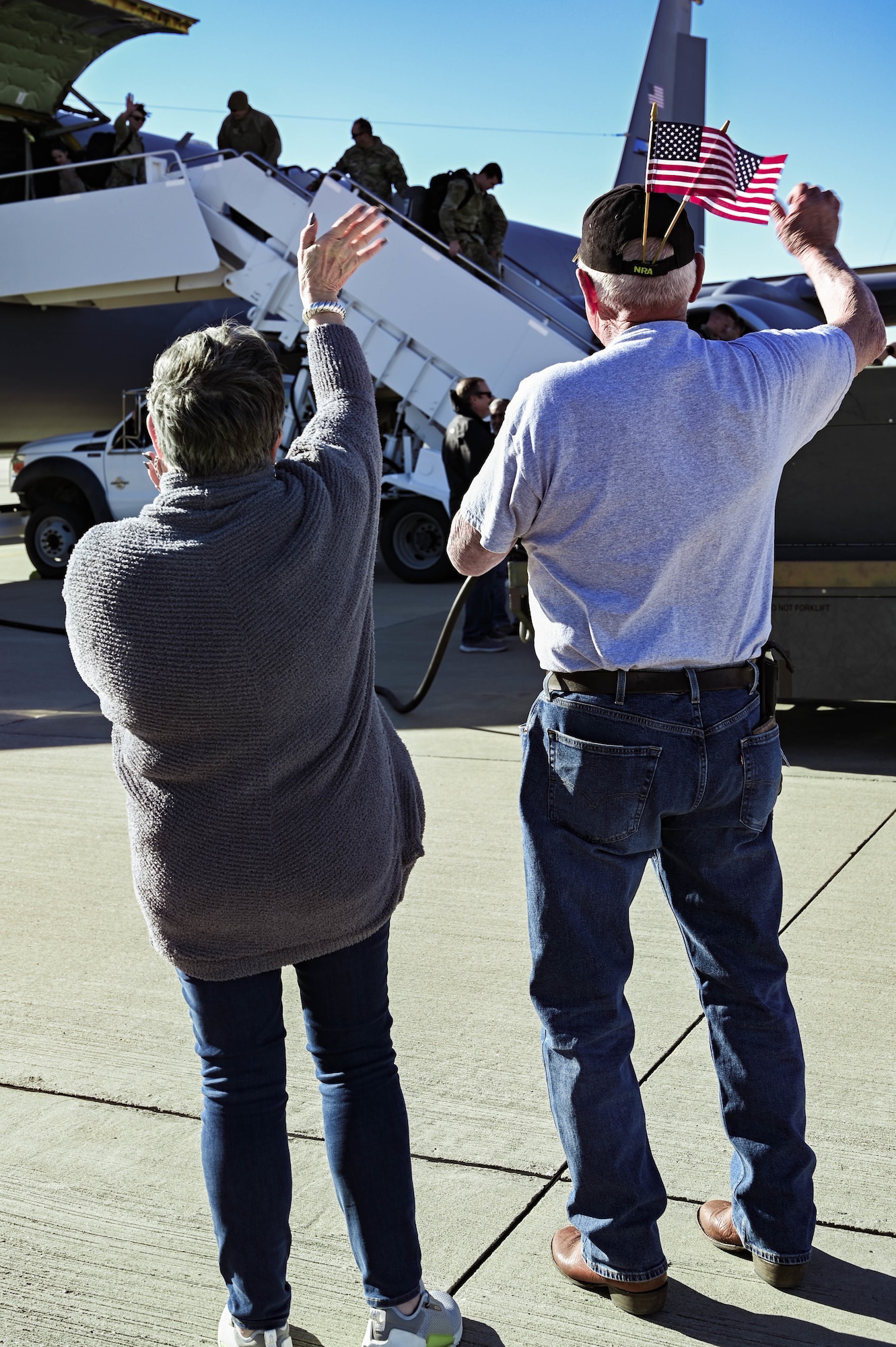 A man and woman waving to someone exiting a plane