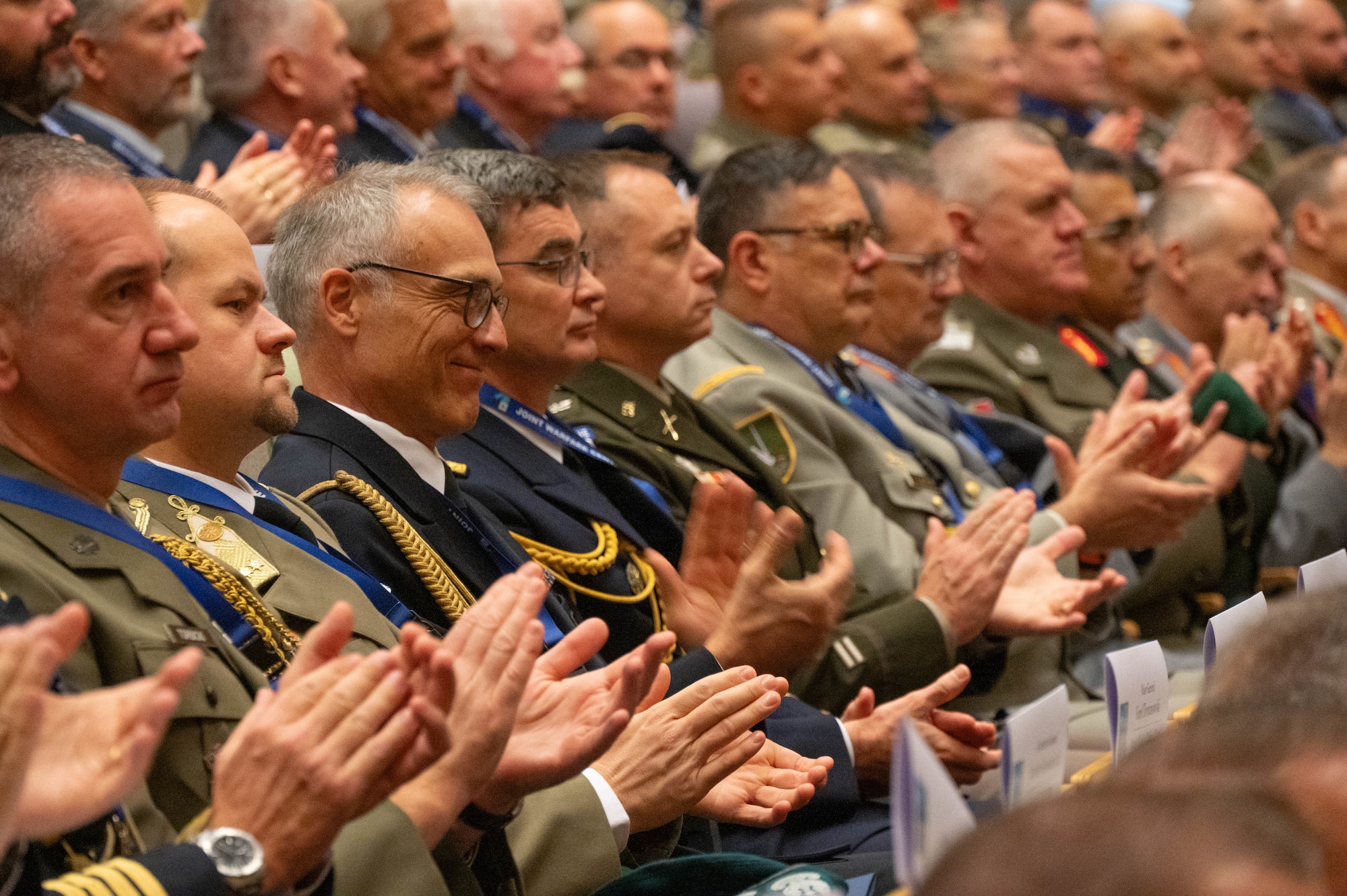 Military and civilian dignitaries applaud during a presentation.