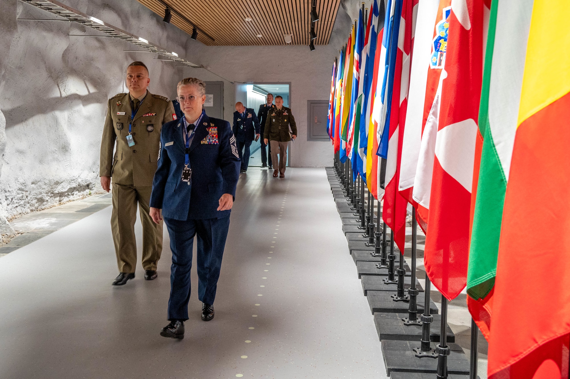 A tour group walks down a hallway near flags from different NATO member countries.