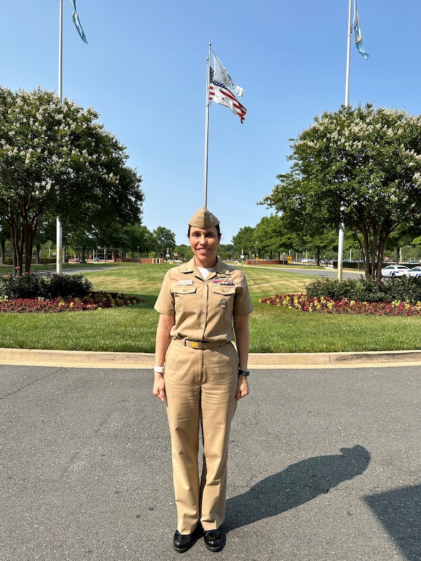 Woman in khaki clothes stands outside in front of a flagpole