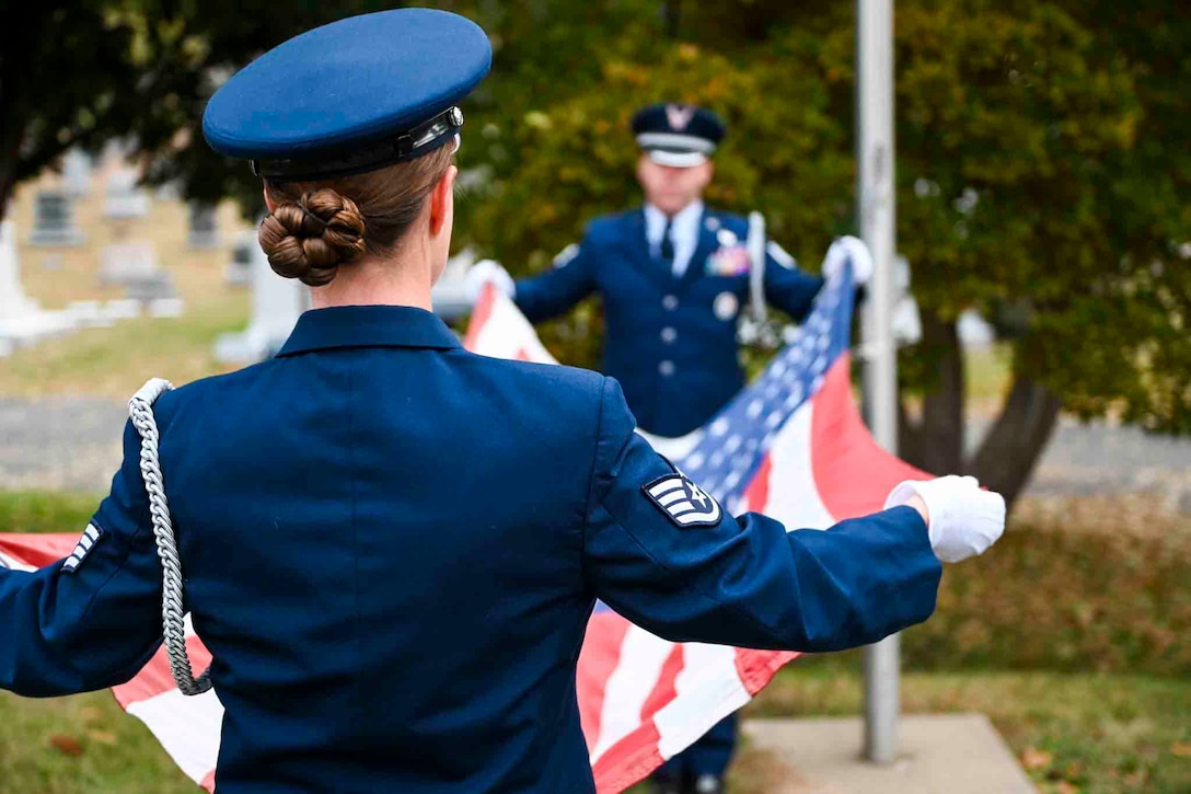 Two airmen stand across from each other while holding an American flag.