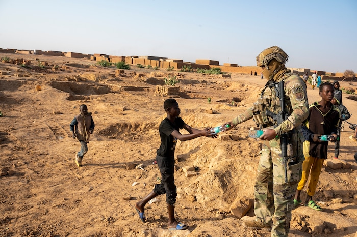 U.S. Air Force Senior Airman Lorenzo Bennette, 409th Expeditionary Security Forces Squadron, Quick Reaction Force (QRF) member, hands a water bottle to a local child near AB 201, Niger, Jan. 6, 2023. QRF postures in and around the base to be able to rapidly respond to developing hostile threats on or immediately around the base. (U.S. Air Force photo by Master Sgt. Michael Matkin)