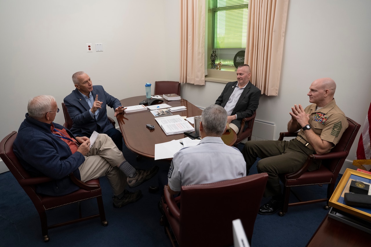 Five men sit around a table engaged in conversation.