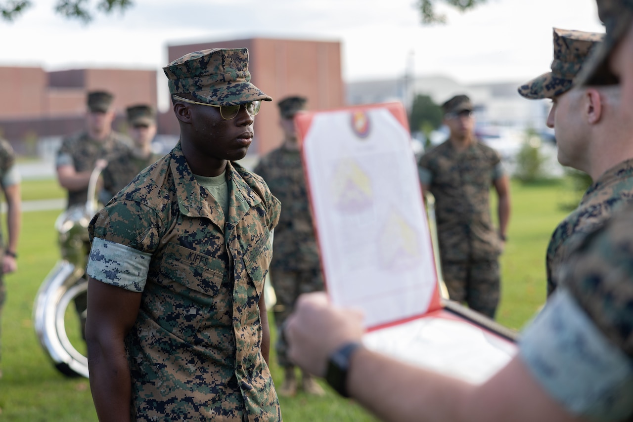 Marines stand at attention outdoors as one reads from a bound document.
