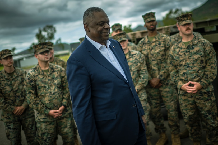 A man in a suit stands with Marines in uniform.