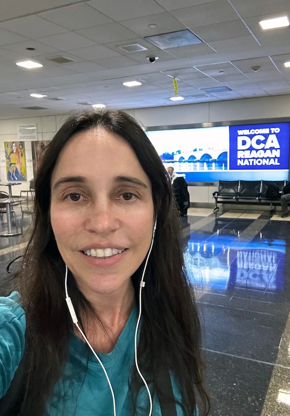 Head and shoulders picture of a woman standing in front of a blue sign in an airport