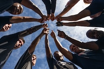 Marines stand in a circle with one arm raised  to the sky.