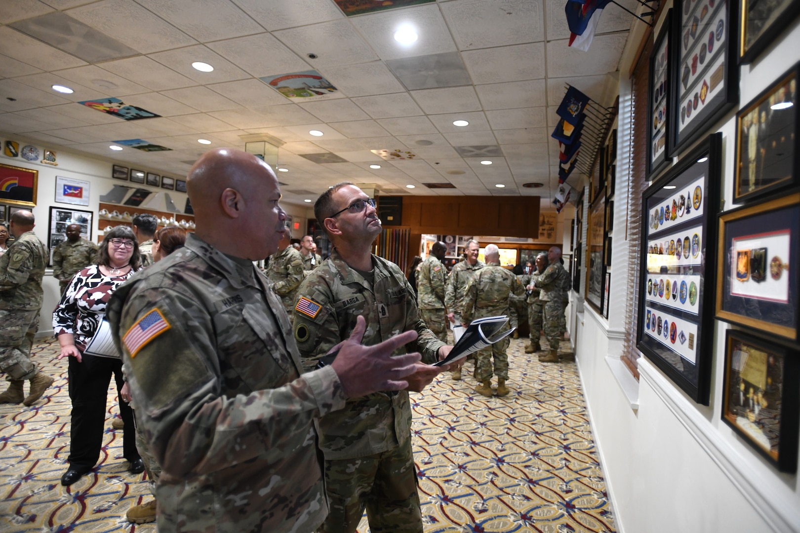 Army Maj. Gen. John C. Harris, the adjutant general of the Ohio National Guard, and Command Sgt. Maj. Scott M. Barga, the command senior enlisted leader of the Ohio National Guard, discuss framed Army patches and unit emblems during the opening ceremony at The 1636 Room at Joint Base Myer-Henderson Hall’s Patton Hall in Arlington, Virginia, Nov. 1, 2023. Named in recognition of the first organized militia in the Massachusetts Bay Colony in 1636 – the predecessor of today’s National Guard – the exhibit space runs the gamut of strategically placed artifacts, framed flags, panel displays, photographs, visual arts and replicated items.