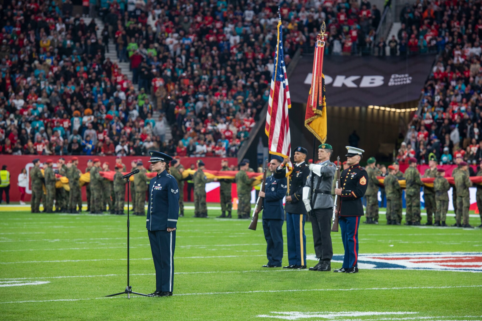 An Airman sings the national anthem with service members in a color guard behind her.