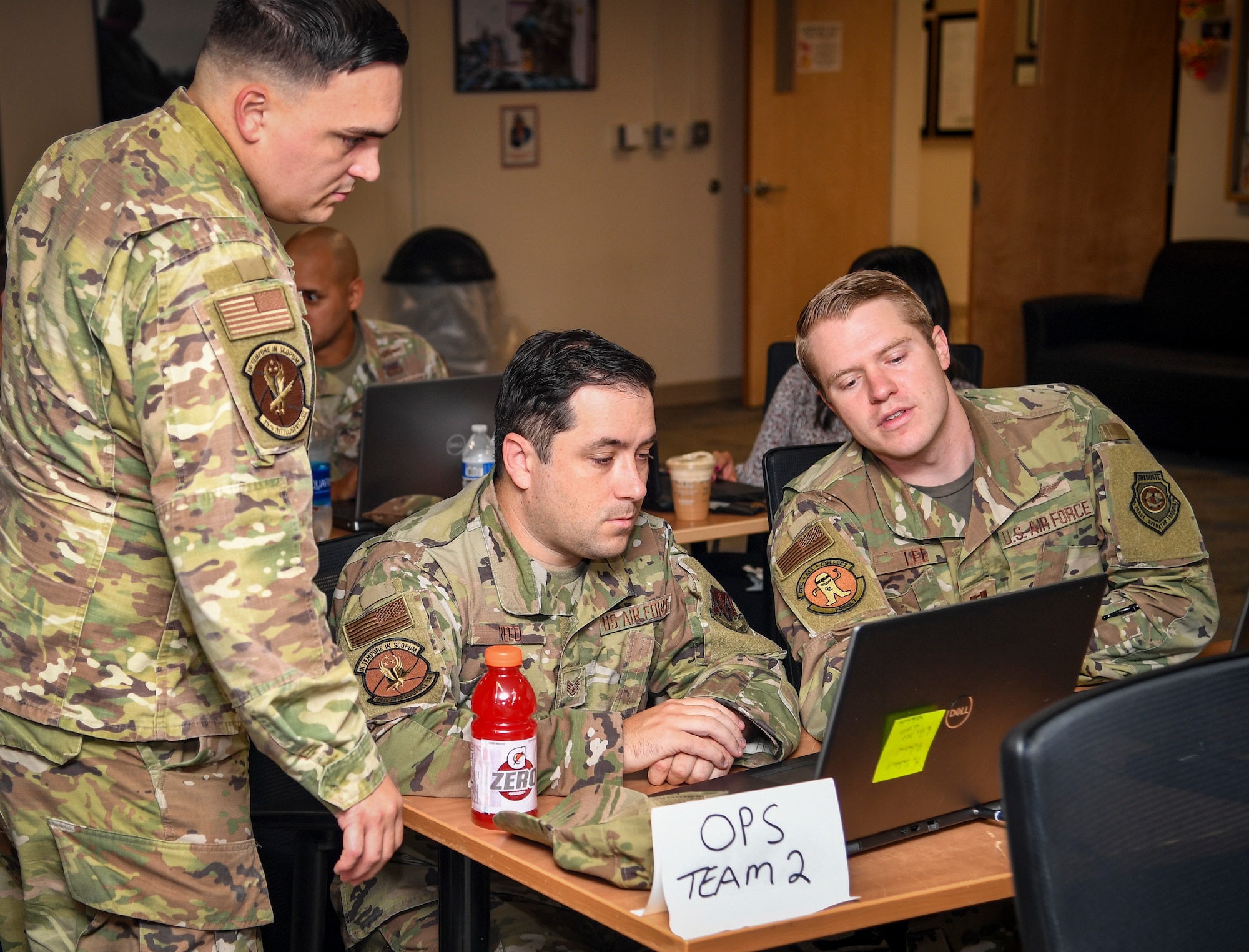 Three guys gather in front of a laptop and discuss information.