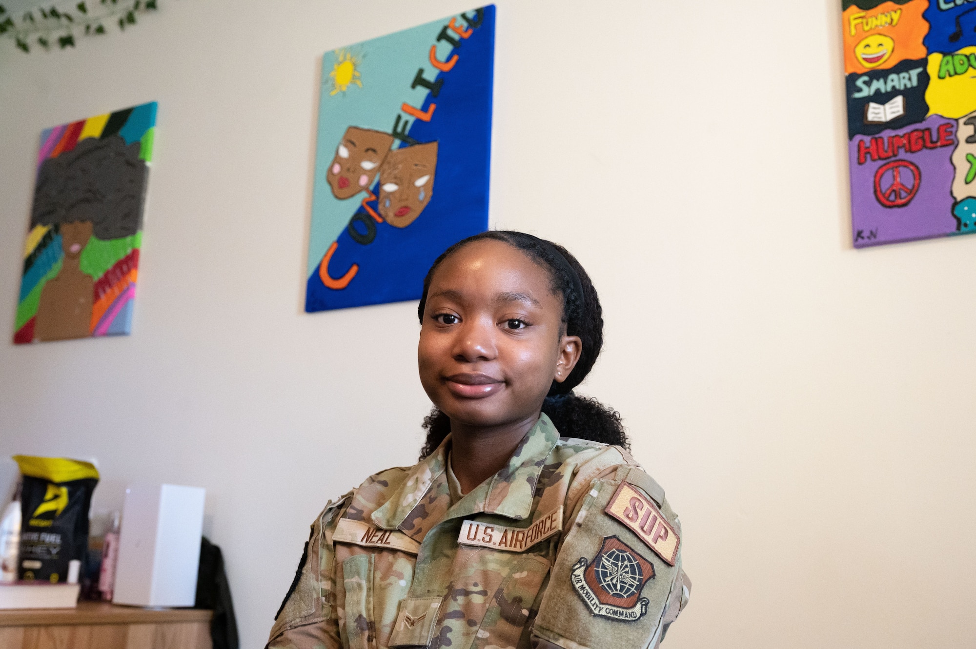 Airman 1st Class Karmella Neal, 436th Logistics Readiness Squadron aircraft parts apprentice, poses for a photo in front of three pieces of her own artwork at Dover Air Force Base, Delaware, Oct. 12, 2023. Neal’s intense emotions can be seen in her artwork and it can take her up to a week to complete her pieces.  (U.S. Air Force photo by Airman 1st Class Dieondiere Jefferies)