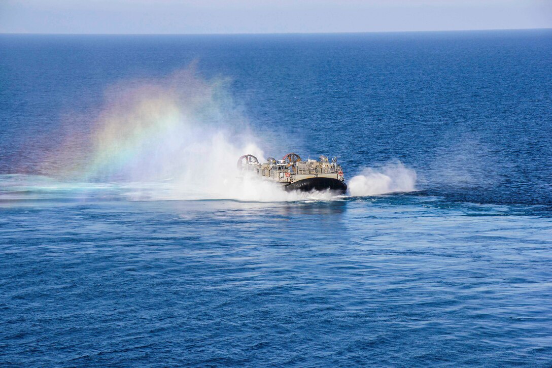 A rainbow appears to the left of a boat transiting a body of water.