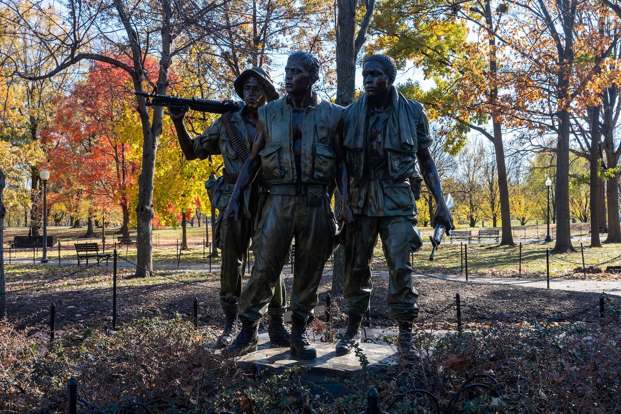 A statue depicts three people standing near each other. One holds a rifle over their shoulders.