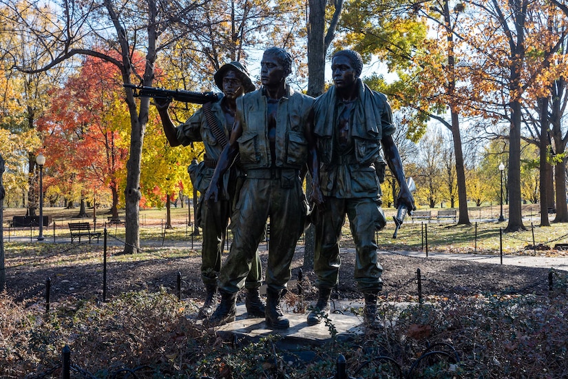 A statue depicts three people standing near each other. One holds a rifle over their shoulders.