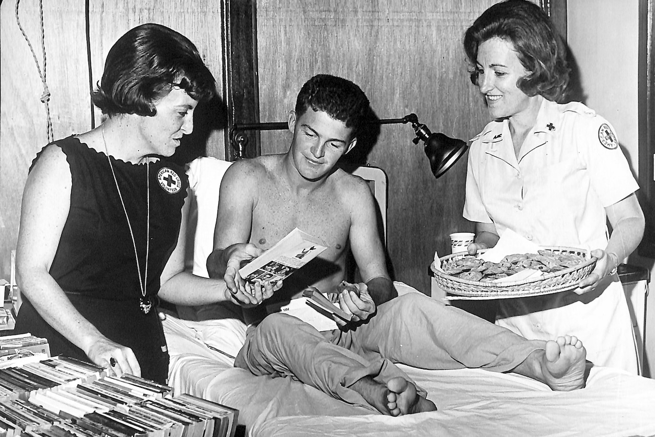 Two people had another person in a hospital bed books and cookies.