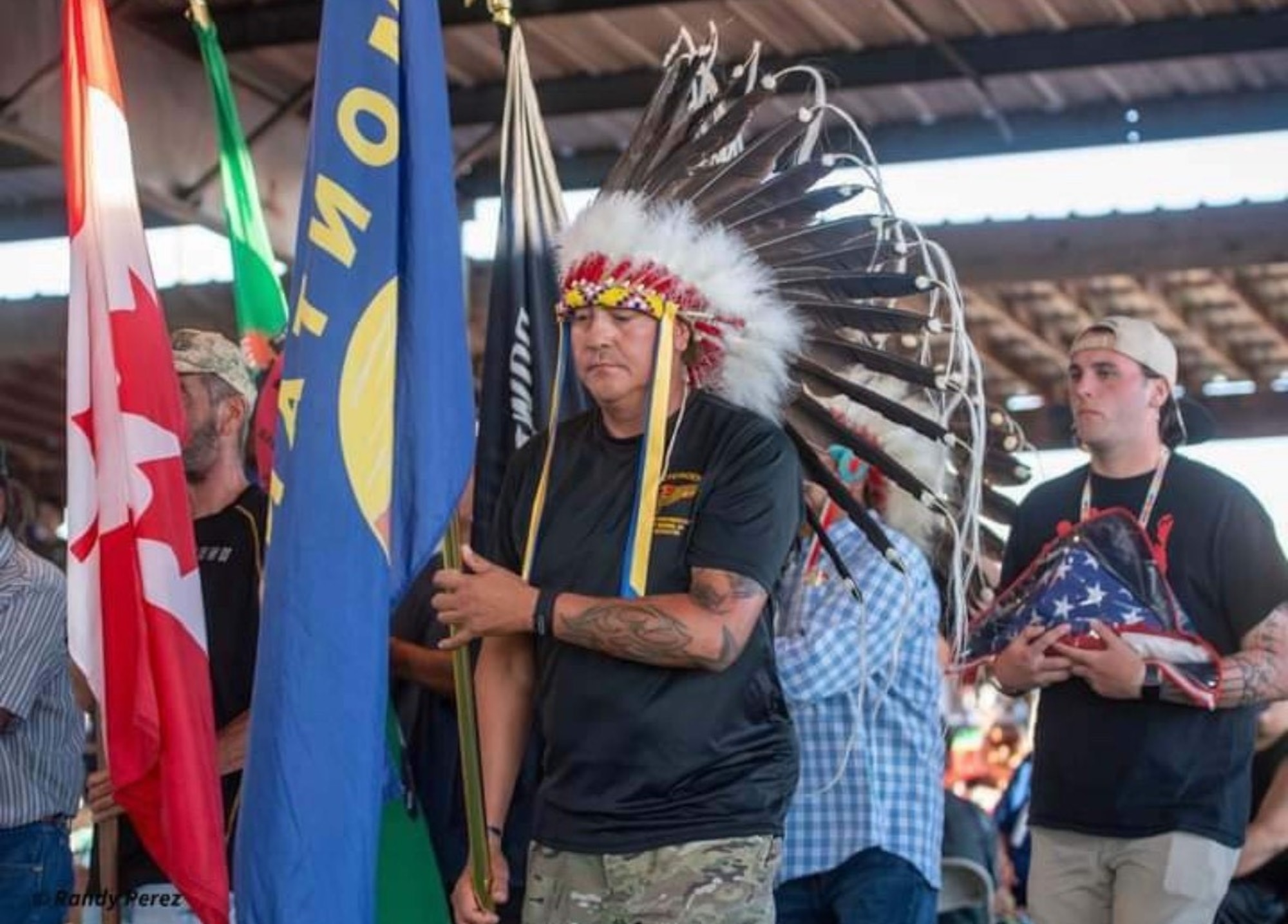 A man wearing a feathered headress holds the Montana state flag and marches towards the left side of the photo.