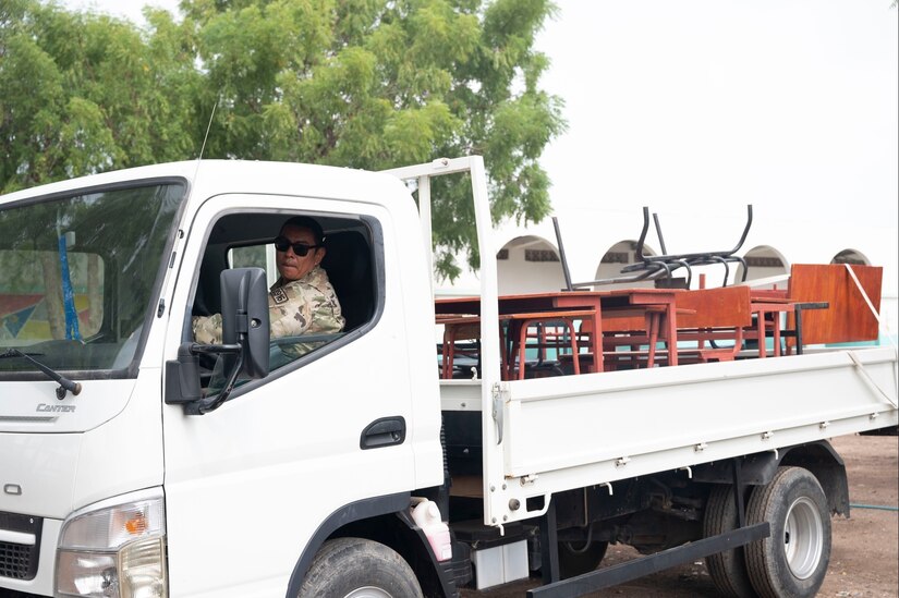 A soldier drives a truck carrying classroom supplies.