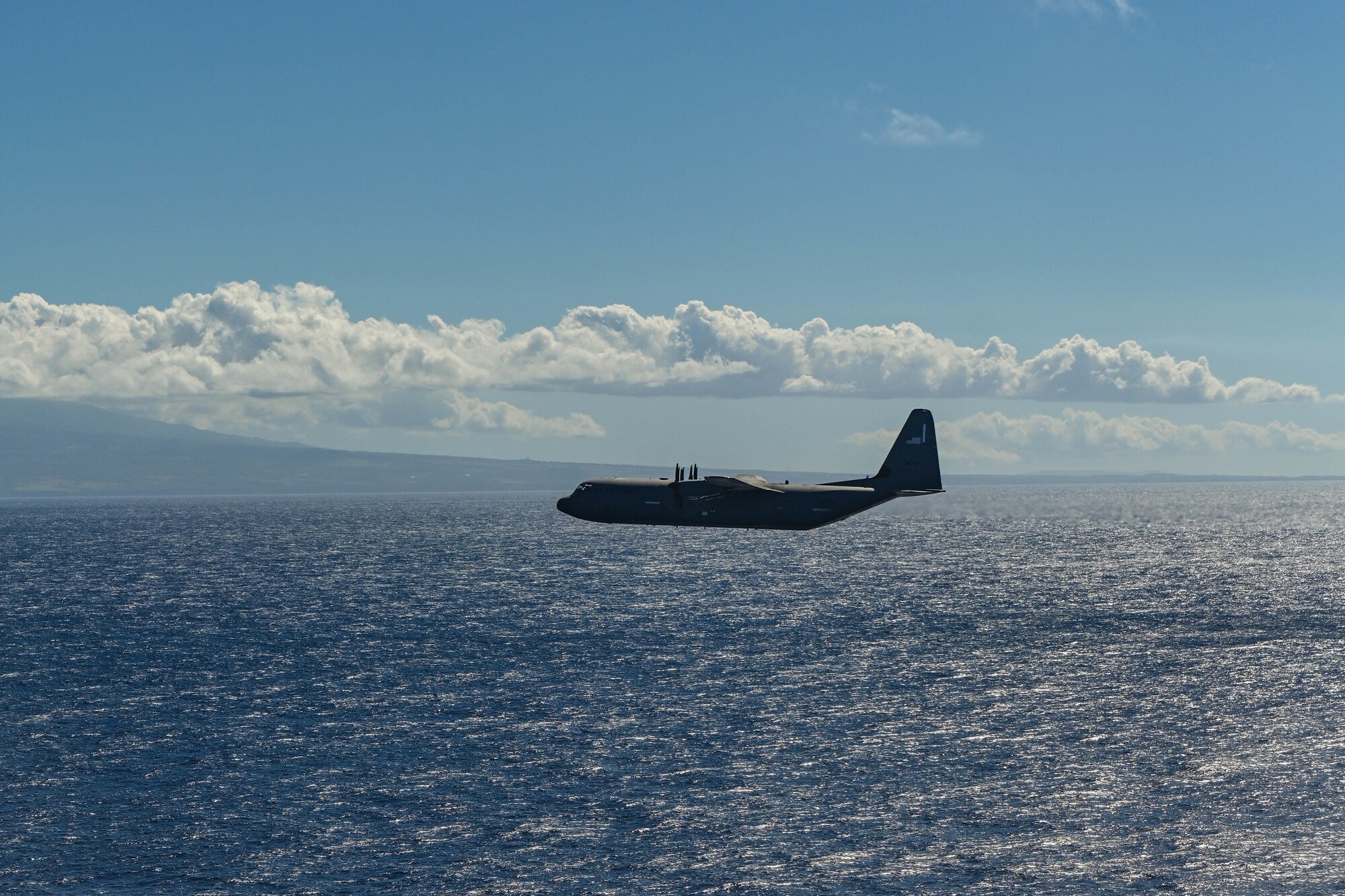 A C-130J aircraft soars over open waters.