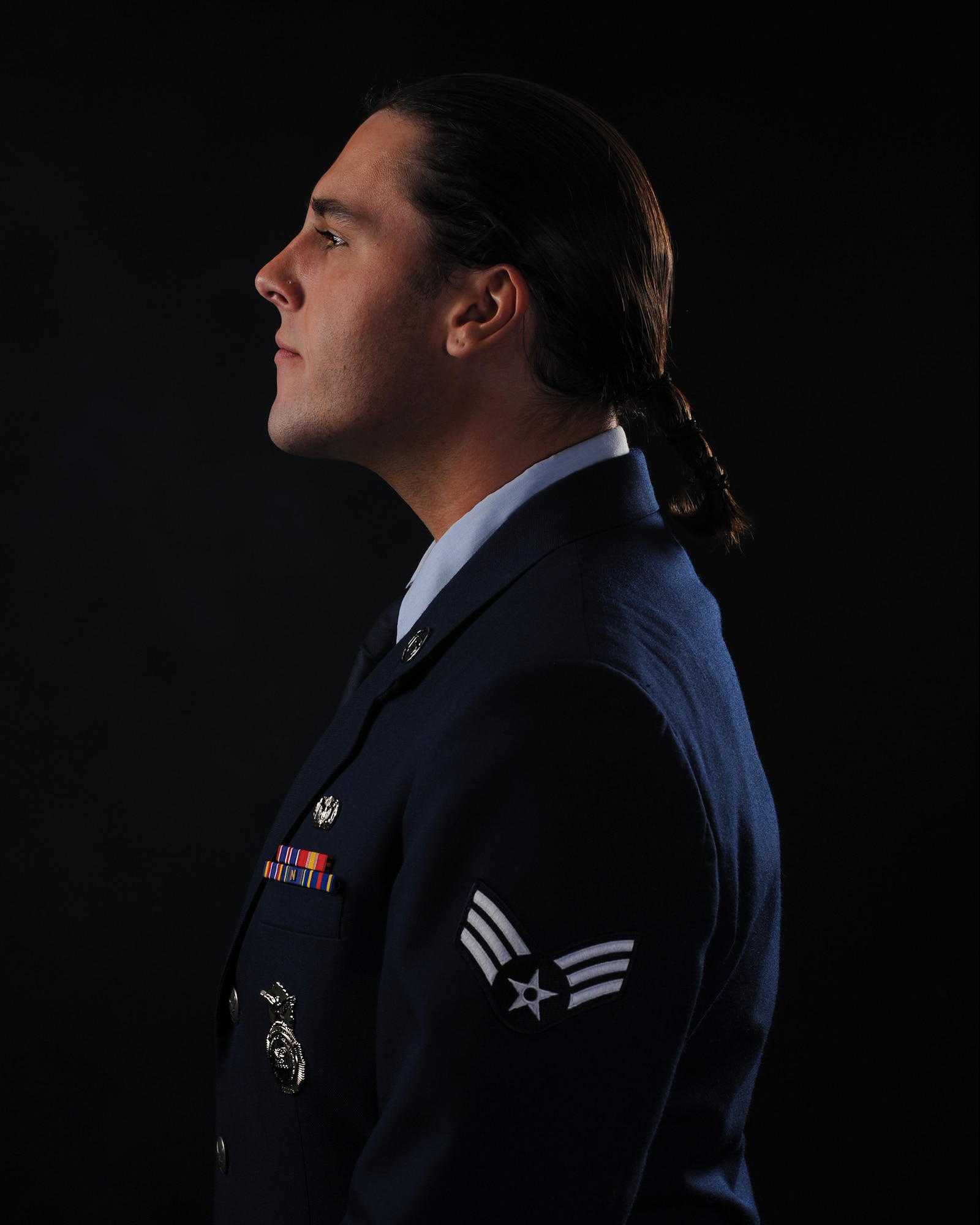 The side profile of a man in dark blue military service dress, with a braid growing just past the bottom of his collar.