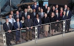 About 20 people in business attire stand in a group by a railing.