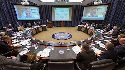 People sit at a round table with three big screens in the front of the room