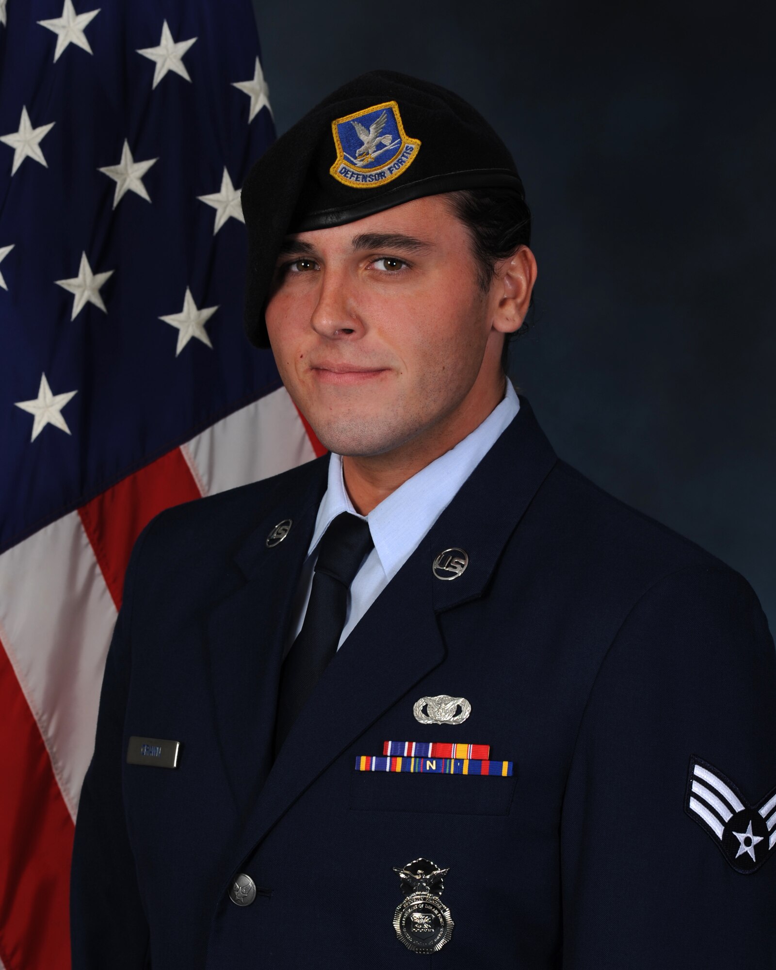 A man in blue military service dress and a maroon security forces beret stands for a stoic portrait against a U.S. flag.