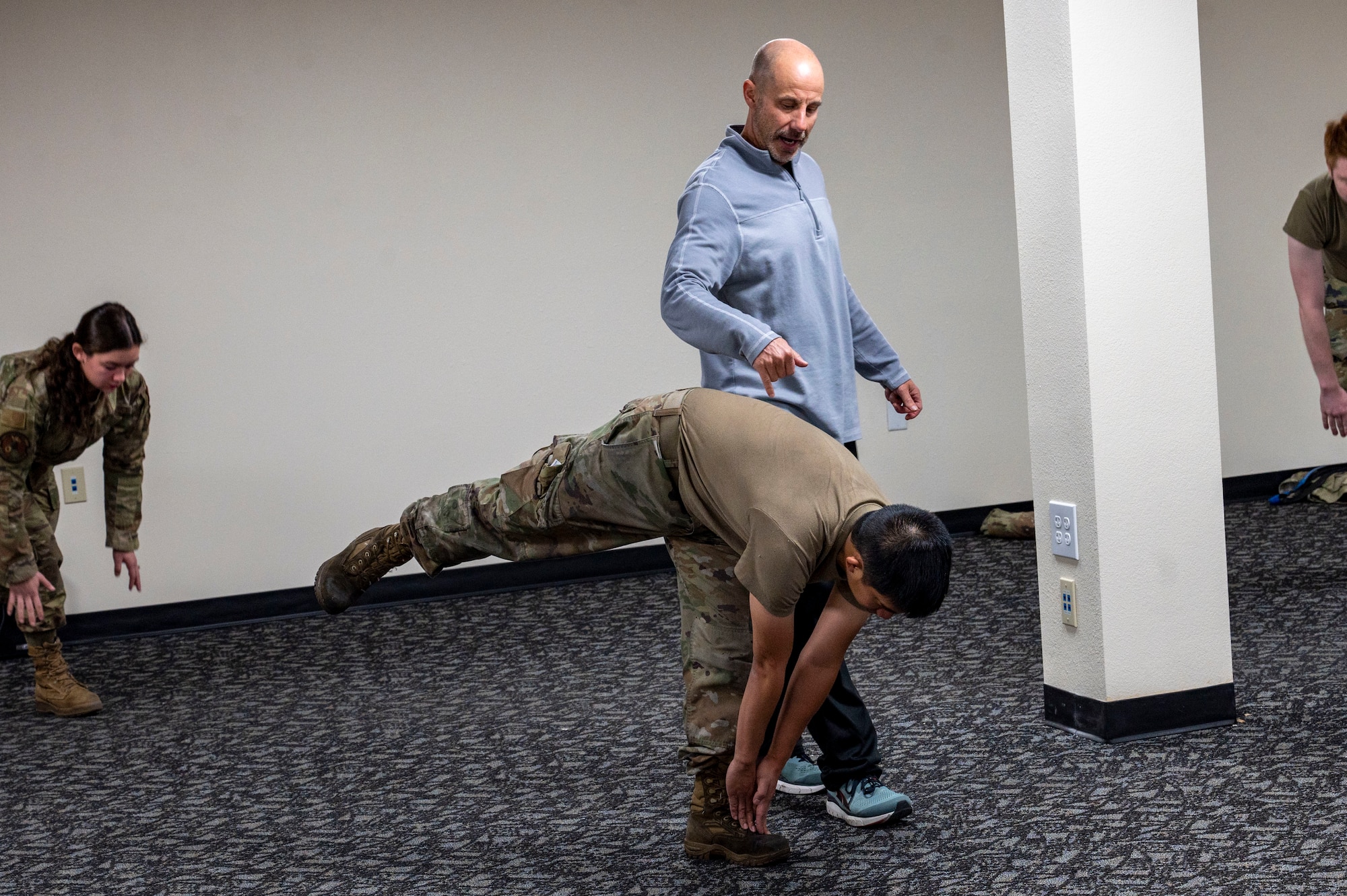 A man assists an Airman while doing a stretch.