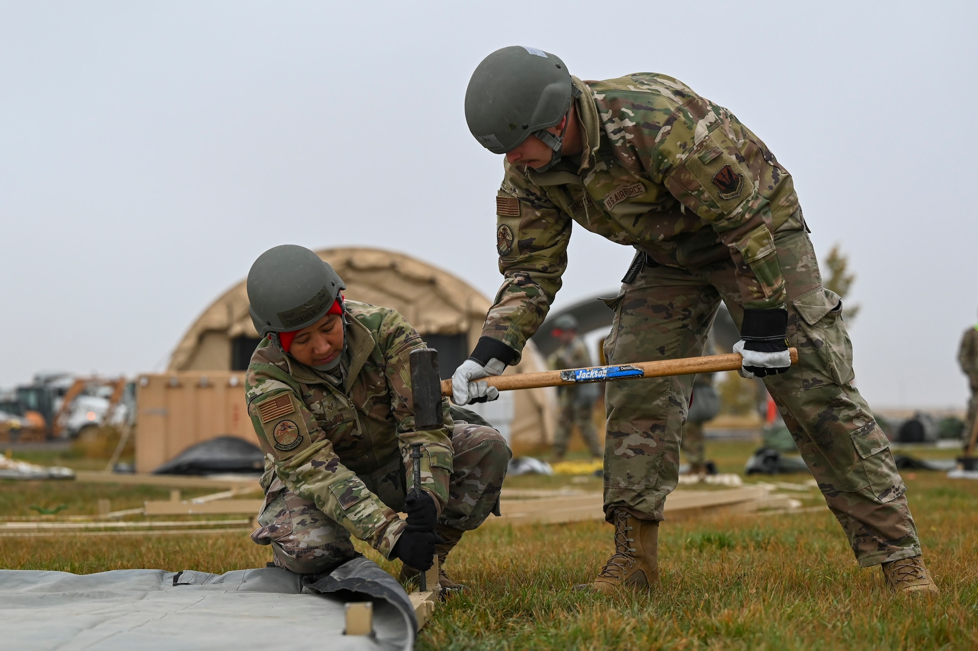 One person squatting and holding a nail in place while the second person hammers it in.